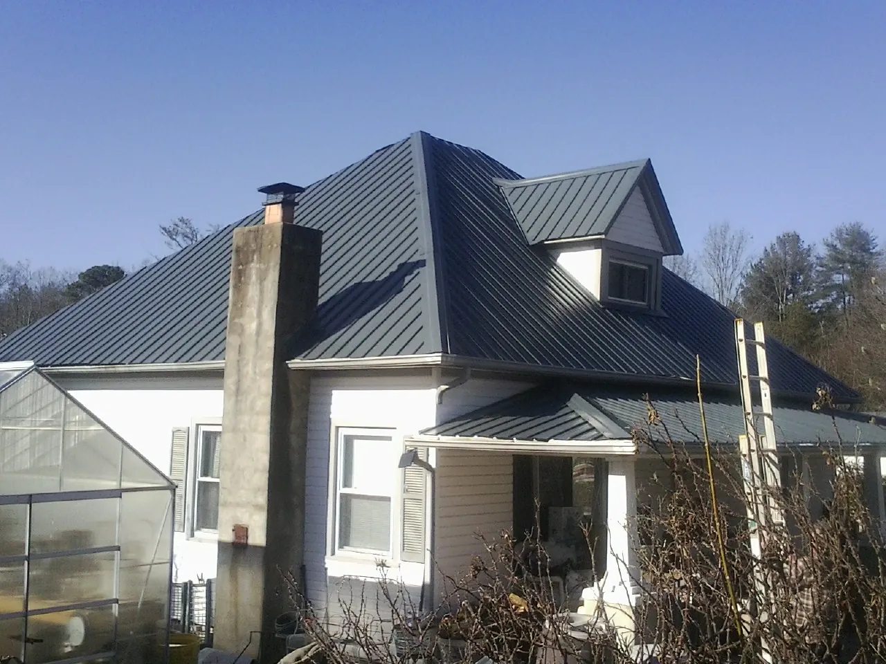 Dark blue standing seam metal roof on a white farmhouse with dormer — Slate & Tile Roof Repair by Roofing Brothers in Mc Kenzie