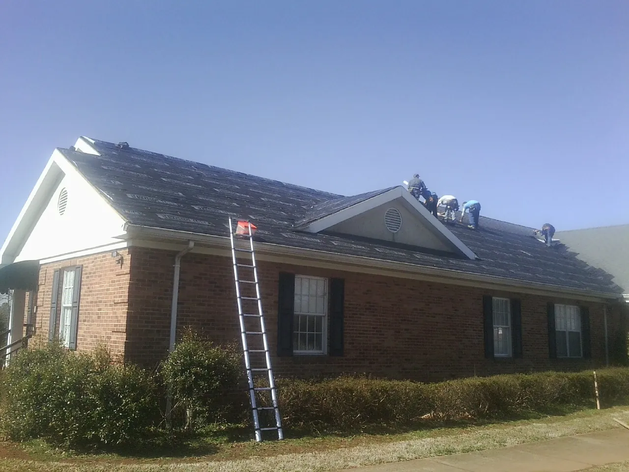 Crew tearing shingles off a brick ranch roof with a ladder set — Emergency Roof Repair work by our crew in Mc Kenzie