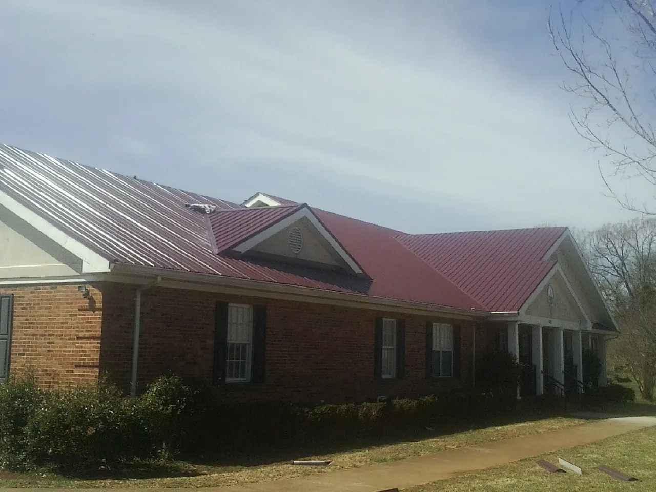Red metal roof with gabled entries on a long brick building, from a Hail Damage Roof Repair job in Mc Kenzie