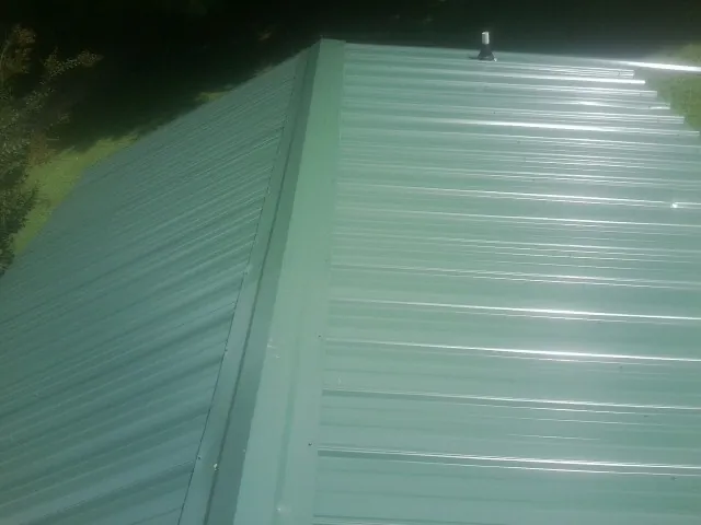 New green metal panels meeting at the ridge of a roof — Flat Roof Repair work by our crew in Mc Kenzie