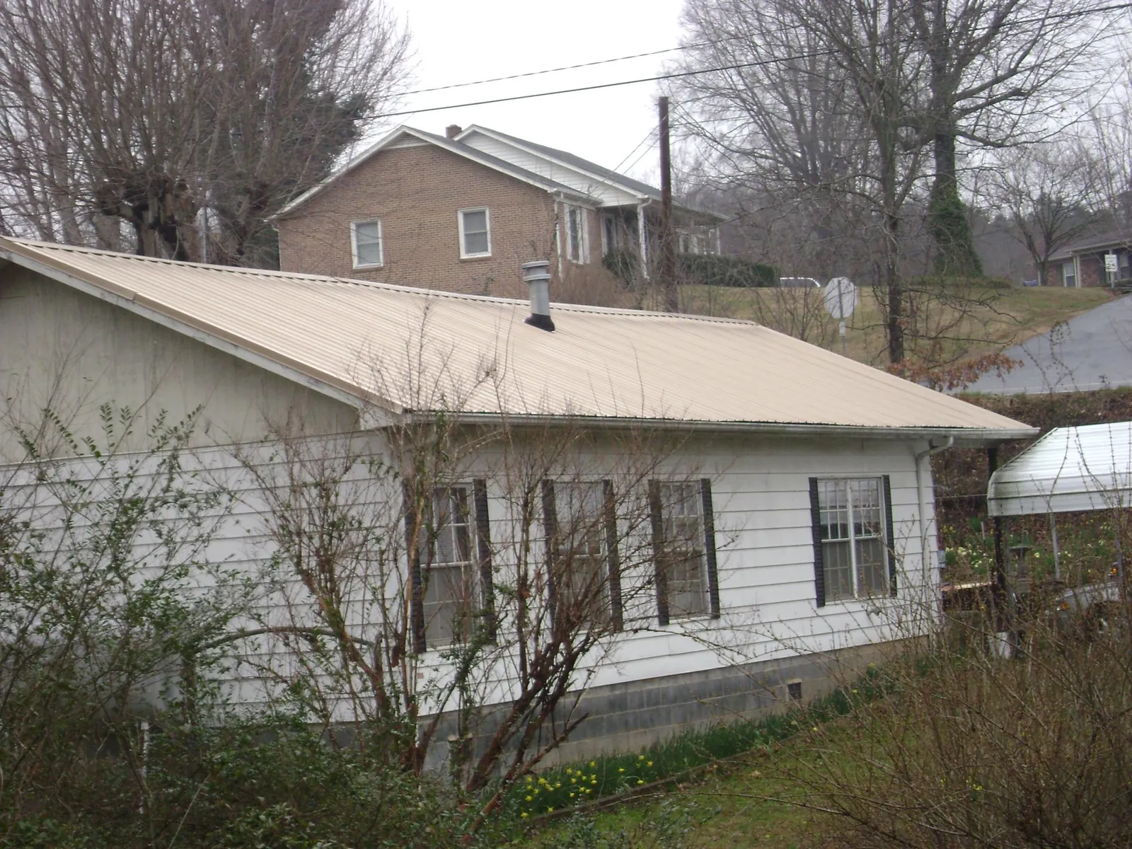 Tan metal roof on a white sided house set into a hillside — Commercial Roofing by Roofing Brothers in Mc Kenzie