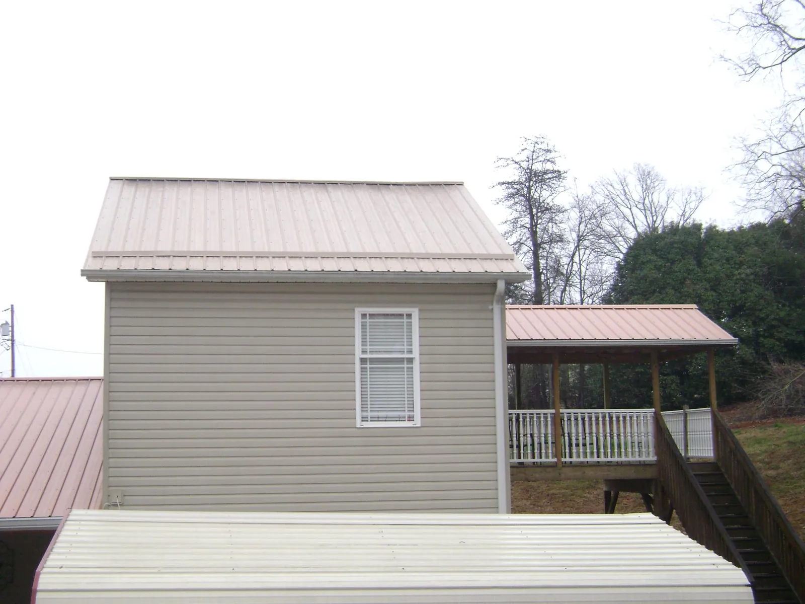 Tan metal roofs on a two story addition and attached porch, from a Roof Replacement job in Mc Kenzie